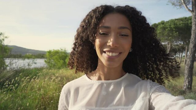 African-American beautiful blogger curly girl looking at camera talking and waving a hand in video call showing in social network streaming video her paradisiac resort of vacations to followers