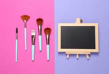 Makeup brushes and chalk board on pink purple background. Copy space