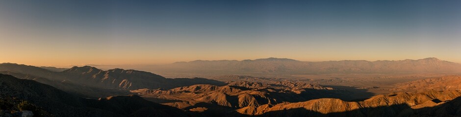 Naklejka na ściany i meble Panorama shot bare desert hills and valley at morning sun and dust in joshua tree national park in america