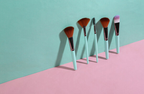 Beauty and fashion minimalistic scene. Makeup brushes on blue pink pastel background with trendy shadows. Creative layout