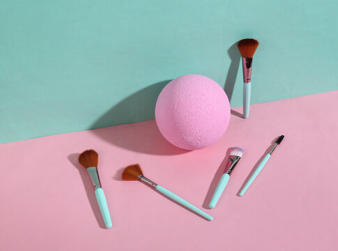 Beauty and fashion minimalistic scene. Makeup brushes with ball on blue pink pastel background with trendy shadows. Creative layout