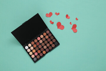 Eyeshadow makeup palette and hearts on blue background. Beauty, love, glamour scene. Top view