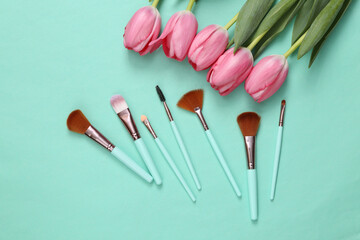 Obraz na płótnie Canvas Make-up brushes and pink tulips on blue background. Romantic, beauty concept
