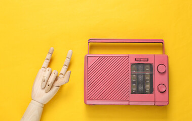 Fm radio and wooden hand showing Rock gesture on yellow background. Top view. Minimalistic music...