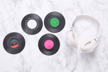 White stereo headphones and vinyl records on a marble surface. Top view