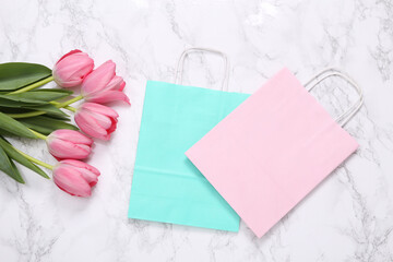 Shopping bags and pink tulips on marble surface. Romantic, beauty concept