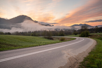 An asphalt road in the mountains during a beautiful, foggy and sunny morning