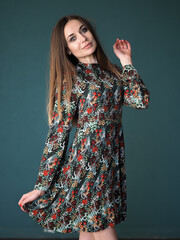 Brunette on a green background stands in a floral dress