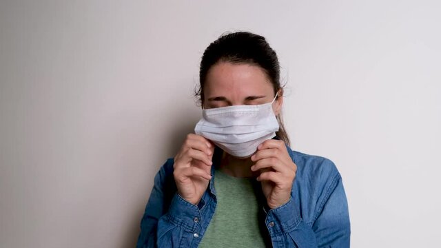 Young pretty Caucasian girl puts medical protective mask on her face and sighs heavily. Woman has contracted viral disease and does not want to infect others. 4k high quality footage.