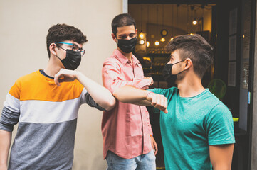 Young friends bump their elbows to greet in time covid-19. They use the mask to defend themselves from the coronavirus. Concept of social distance and friendship.