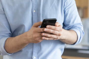 Close up cropped of businessman holding smartphone, typing on screen, writing message in social network or browsing mobile device apps, young man scrolling, chatting with business partner online
