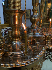 Fototapeta na wymiar Fire of candles at the iconostasis in a Christian church. Сandlestick in the church. Lighting candles in the Church. Old style gilding holder. Gilded church altar utensil around it. Close up photo.
