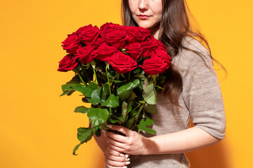 The girl has a bouquet of scarlet roses in her hands. Yellow background. Space for the text. Selective focus.