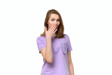 Fototapeta premium Young woman covering mouth with hand, looking serious, promises to keep secret. . Studio shot, white background