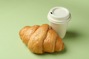 Croissant and paper cup on green background