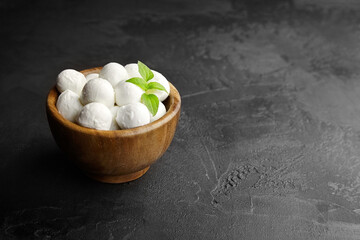 Mini mozzarella cheese balls in wooden bowl on black stony background