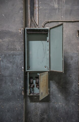 Empty old switchboard. Open distribution panel box on damaged concrete wall in abandoned building