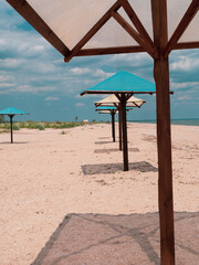 Wooden umbrellas on white sand beach with harsh shadows, vivid blue sea water cloudy sky background. Scenic landscape wallpaper summer vacation seasonal tropical marine travel rest resort advertising.