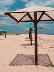 Wooden umbrellas on white sand beach with harsh shadows, vivid blue sea water cloudy sky background. Scenic landscape wallpaper summer vacation seasonal tropical marine travel rest resort advertising.