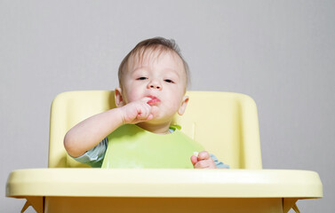 little child eats on gray background, child puts his finger in his mouth