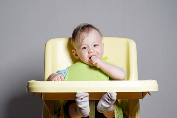 little child eats on gray background, child testing food, looking at camera