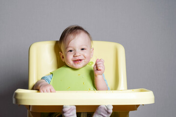 little child eats on gray background, child testing food, looking at camera and smiles