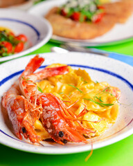 Italian ravioli with big cooked shrimps served on a white plate over bright green background.
