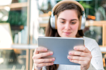 Young woman talking in video chat with her friend via digital tablet while sitting in street cafe.