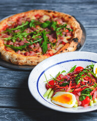 Tuna salad with vegetables, boiled eggs, cherry tomatoes and spices. Pizza with salmon fish, cheese and fresh arugula