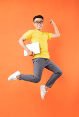 Asian man in yellow t-shirt jumping on orange background