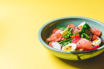 Salad with spinach, eggs and radish in a bowl over bright yellow background.