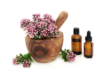 Oregano herb flowers & leaves in a mortar with pestle with essential oil bottles used in herbal...