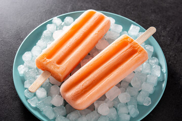 Orange popsicles on blue plate on black background
