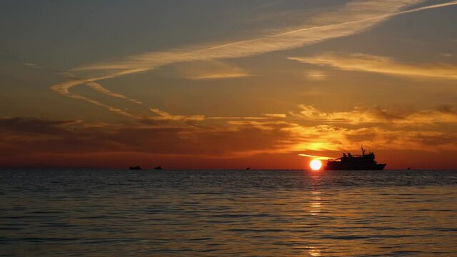 Sunshine on the sea coast, nature is painted in orange shades of the sun. The waves of the sea are splashing. The ferry boat is sailing. Video in 4K.