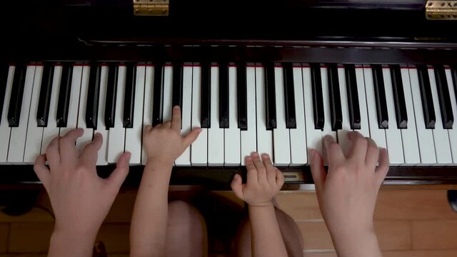 Toddler playing piano with adult, four hands, piano duet.