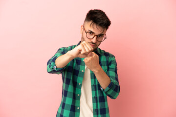 Young caucasian man isolated on pink background with fighting gesture