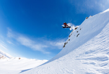 Snowboarder jumps off a cliff against a blue sky