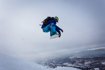 Snowboarder jumps in the mountains against the blue sky