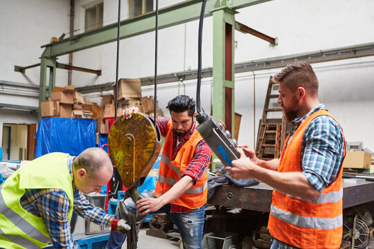 Team in der Fabrikhalle befestigt Last an Kranhaken