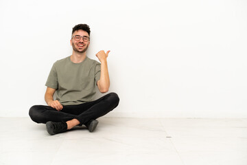 Young caucasian man sitting on the floor isolated on white background pointing to the side to present a product