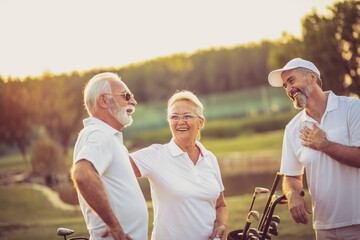 Three seniors golfers talking on golf field.