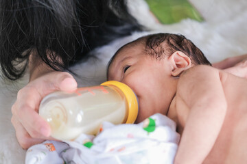 The baby drinks from the bottle that the mother feeds.