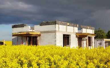 Fototapeta na wymiar Rural single family house under construction with rapeseed field in foreground and stormy clouds in background.