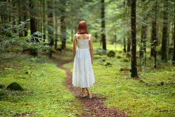 Back view of a woman with white dress walking in a forest