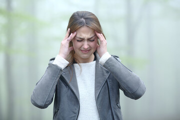 Stressed woman suffering migraine in a foggy forest