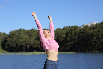 Happy woman raising arms beside a lagoon in the mountain