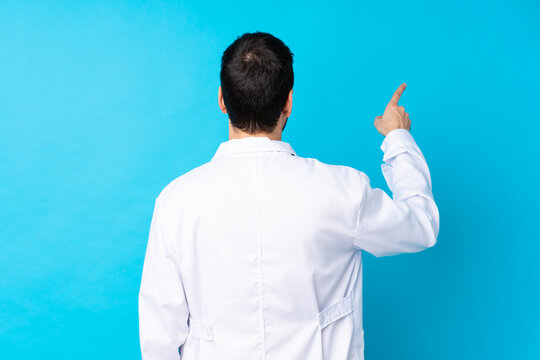 Young Caucasian Man Over Isolated Background Wearing A Doctor Gown And Pointing Back