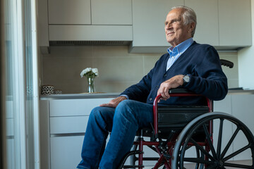 Cinematic shot of elderly disabled senior man in wheelchair is looking through window in the morning at home. Concept of life, pensioner, grandparents, retirement, boarding house, hope, handicap