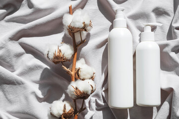 Beauty SPA branding mock-up. Natural organic eco cosmetics. White cosmetic bottles, cotton flowers on gray fabric with sun shadows flat lay top view. Blank label for branding. Eco textiles, mockup