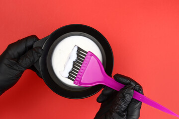 Stylist holds a bowl of hair dye on a red background